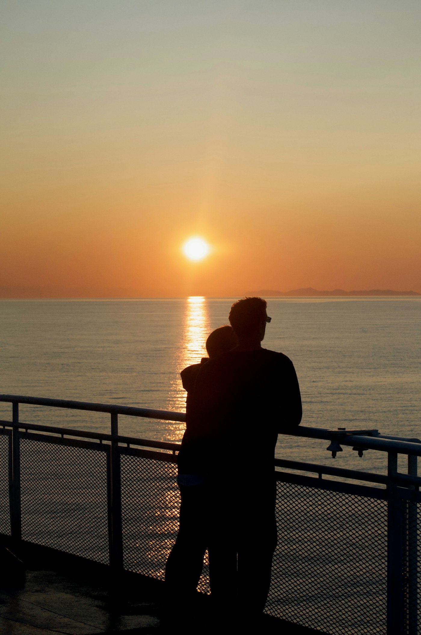 Two people standing on a ship deck at golden hour