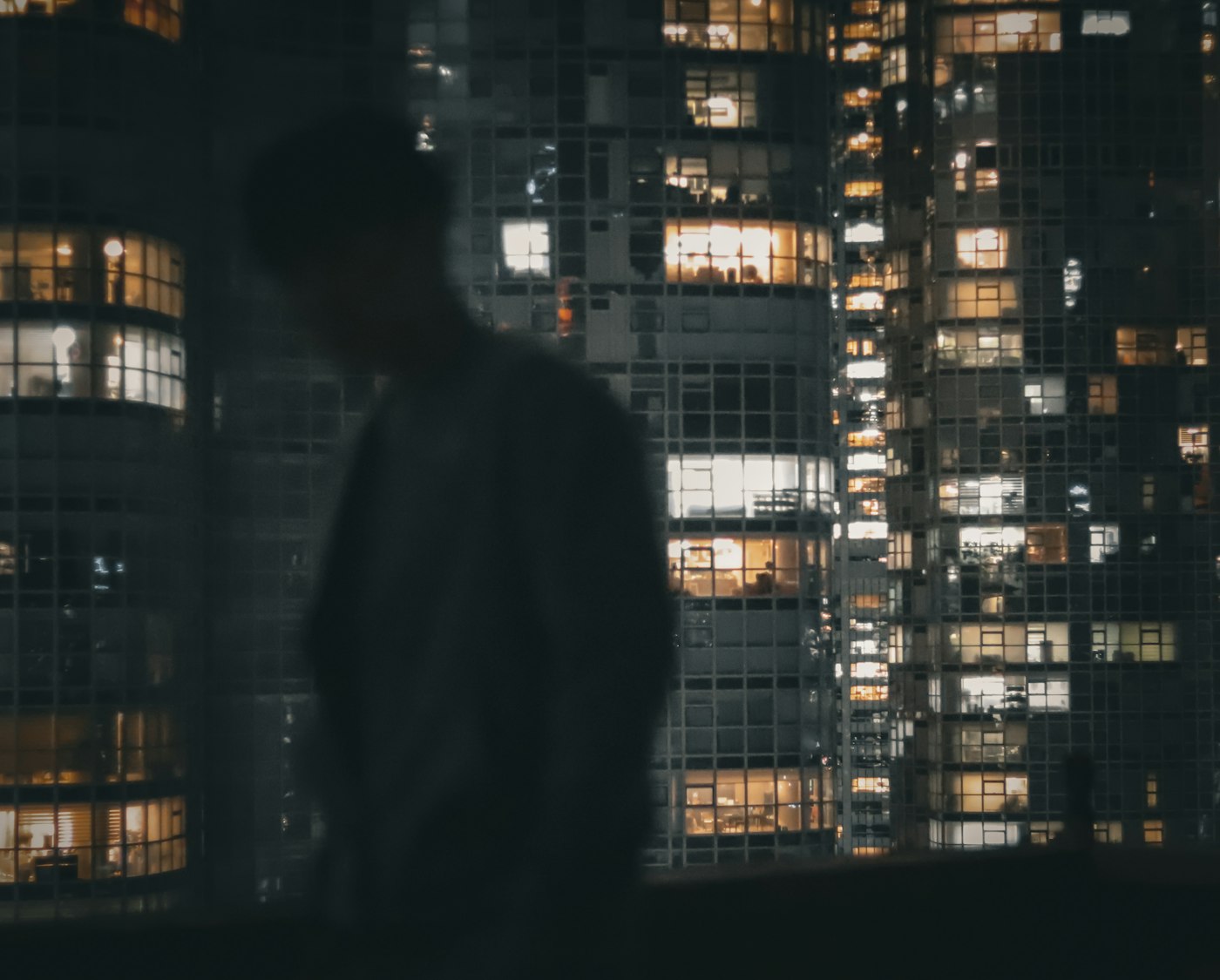 A man in a dark suit standing beside a floor-to-ceiling window overlooking a city at night
