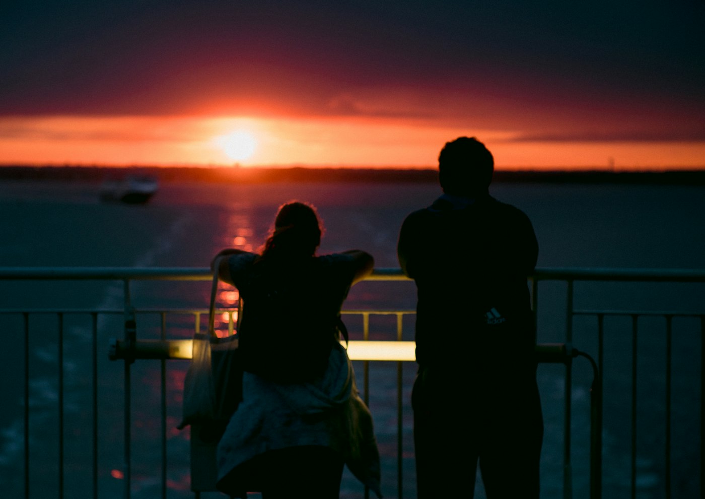 Two people silhouetted against a golden sunset on a ship deck